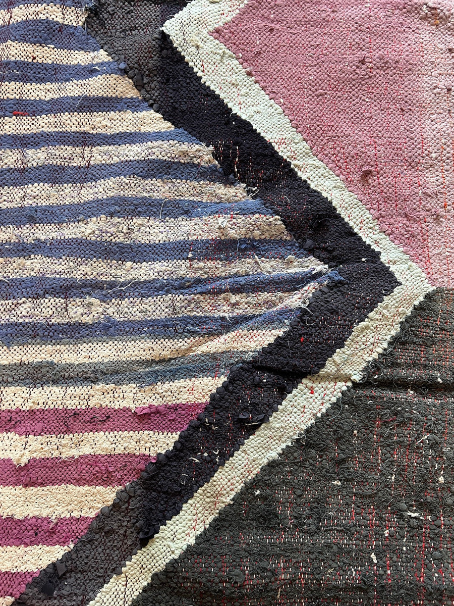 detail Handwoven rag rug with a dynamic diamond and striped design from weavers in southern Morocco. Beautiful on the floor or on the wall. Colors: shades of periwinkle to royal blue, off- white, violet, charcoal, chalky mauve pink, and more. 3" braided  fringe at one end. Note: this rug has some puckering and doesn't lay completely flat. Size: Approx. 4 feet 11" x 8 feet 11" (57" x 107")